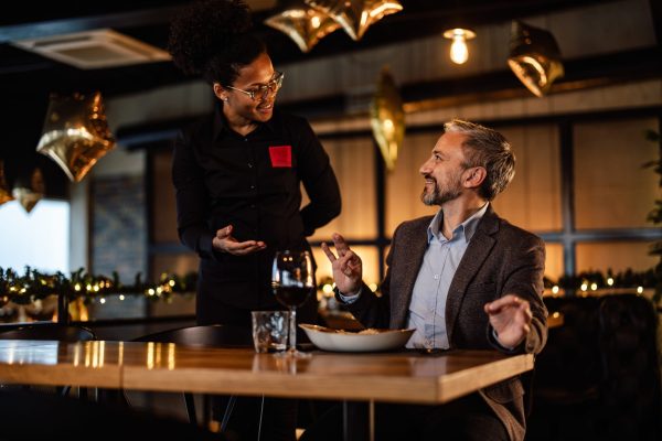 Businessman enjoying dinner, discussing with a waitress amidst festive restaurant decorations.