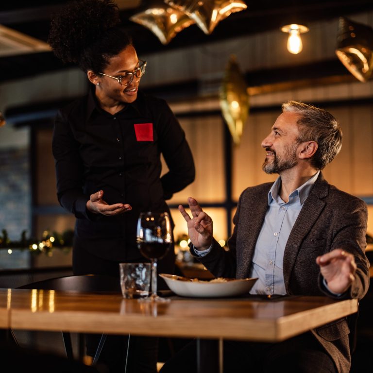 Businessman enjoying dinner, discussing with a waitress amidst festive restaurant decorations.
