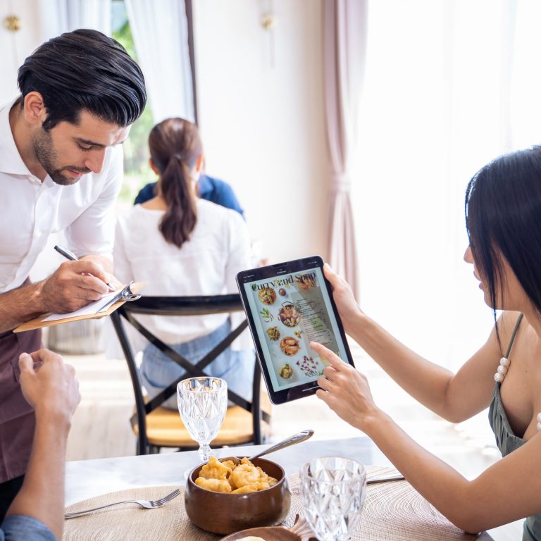 Caucasian waiter receiving order serving from customer in restaurant. Attractive server service man working, taking note, writing order from consumer with pen at table in dining room with happiness.